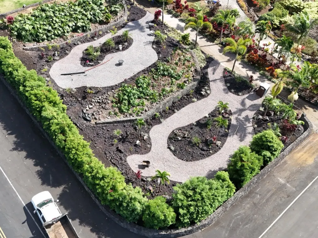 After completion of the project. Gravel pathways, lava rock ground cover, and flowerbeds with native Hawaiian plants are visible.