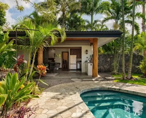 Canoe plants and vibrant tropical foliage surround a luxury swimming pool and open-air patio pavilion for Big Island landscaping.