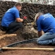 Kailua-Kona landscape workers in blue shirts install edging in dark soil next to a volcanic rock wall, highlighting Hawaii lava vs soil challenges.