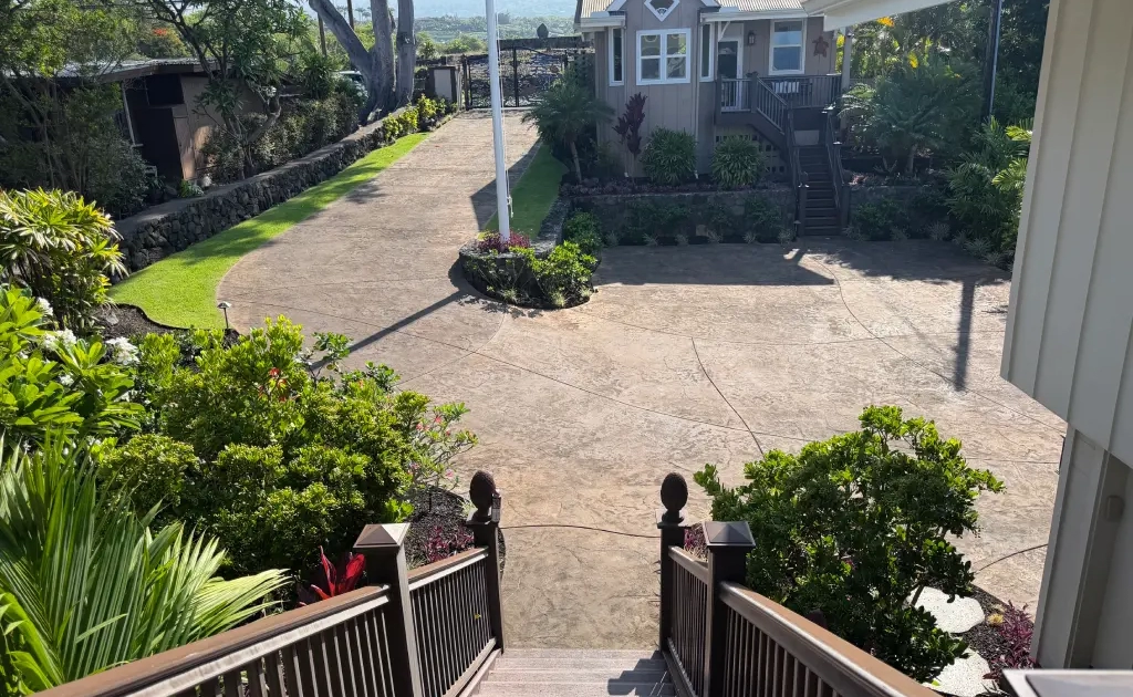 home-landscape-kailua-kona The same Kailua-Kona property after renovation, with a stamped concrete driveway, new lawn, lava rock planter beds, and flagpole between the main house and ohana house.