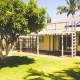 Lush green lawn and mature shade tree beside a sunny Kona home with palm trees, showing healthy summer lawn care on the Big Island of Hawaii.