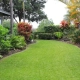 Curved grass lawn bordered by tropical plant beds containing directional sprinkler heads and drip irrigation on a Big Island property.